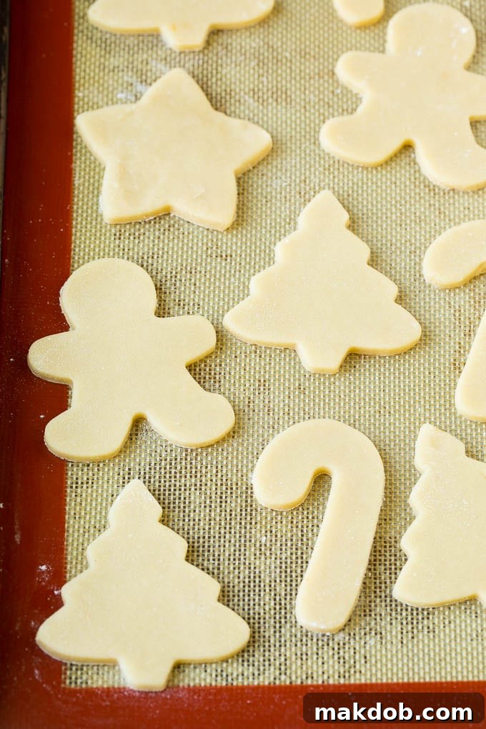 Christmas Sugar Cookies Recipe | Christmas Cookies #cookies #frosting #sprinkles #sugarcookies #christmas #dessert #dinneratthezoo Freshly cut cookie dough in various holiday shapes arranged on a baking sheet, ready for baking.