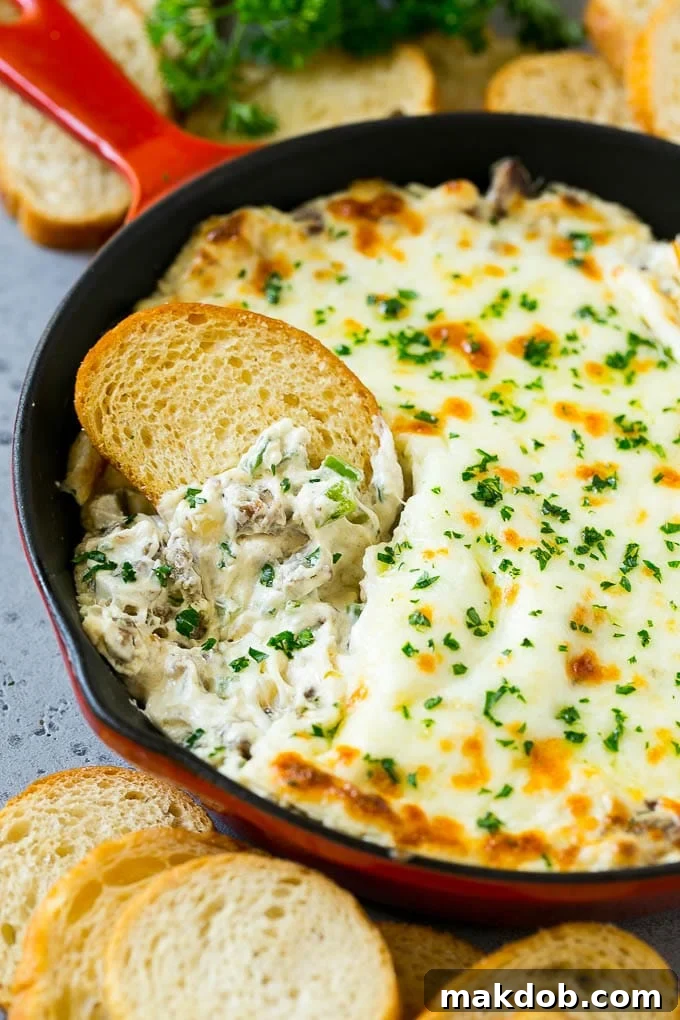 Philly Cheesesteak Dip Recipe | Cheesy Dip | Baked Cheese Dip #steak #dip #appetizer #cheese #dinneratthezoo Philly cheesesteak dip with a baguette piece scooping some dip out.