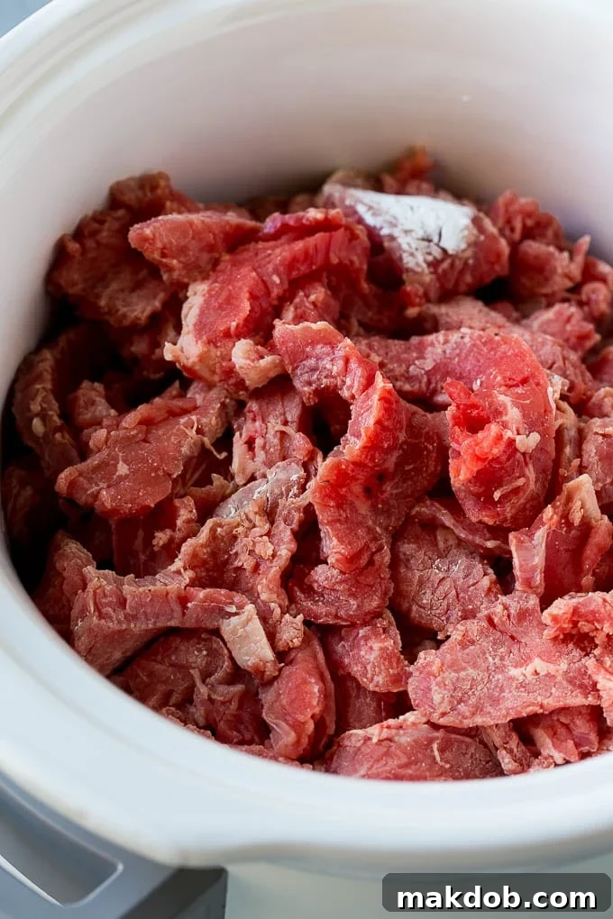 Thin strips of flank steak being tossed with cornstarch inside a slow cooker before adding the sauce.