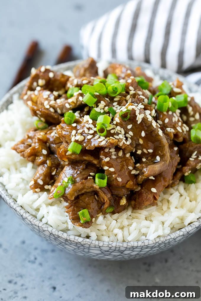 Slow cooker Korean beef generously served over a mound of fluffy steamed rice, garnished with green onions and sesame seeds.