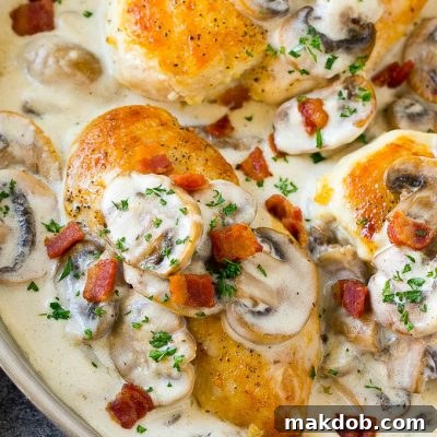 A skillet of mushroom chicken in a creamy sauce, topped with bacon and herbs.
