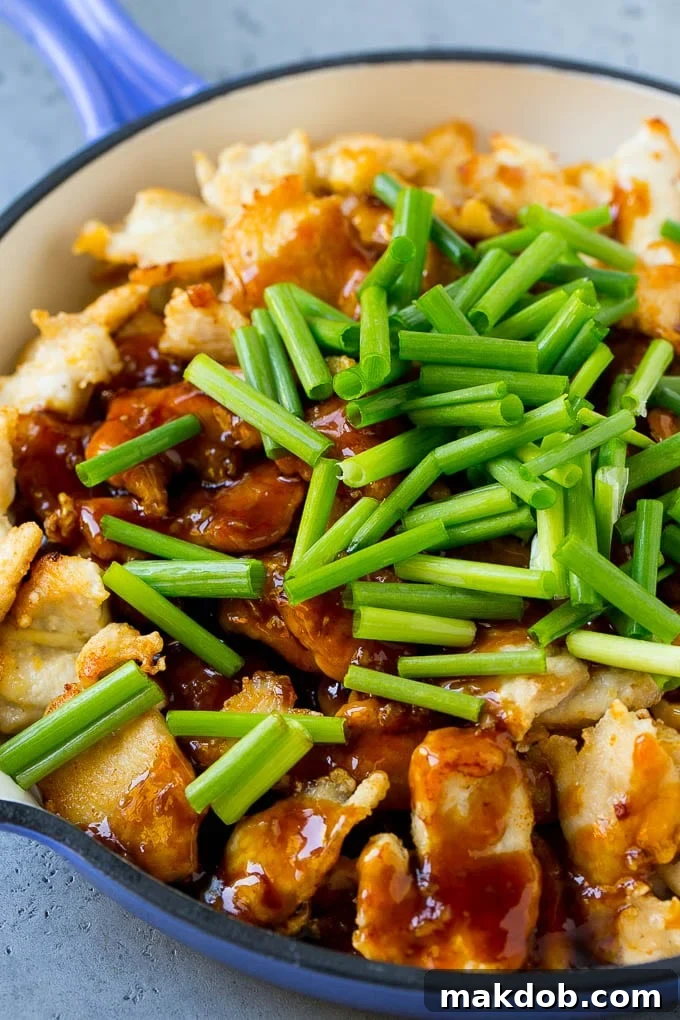 Sliced chicken breast in a skillet, coated with glossy Mongolian sauce and vibrant green onions.