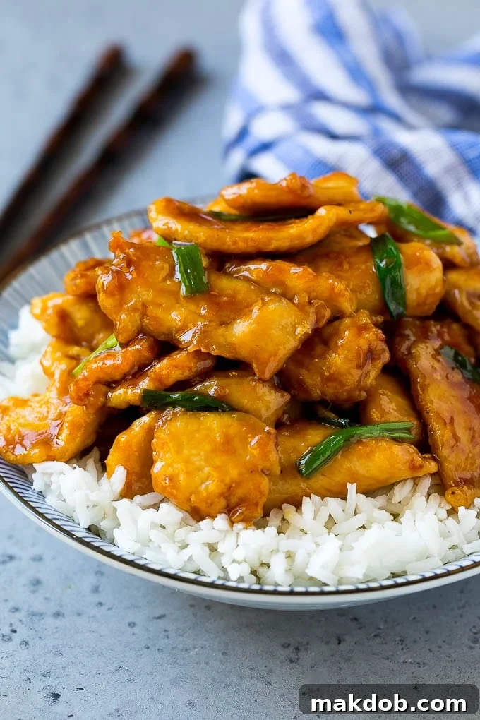 Mongolian chicken served over a bowl of white rice, garnished with green onions.