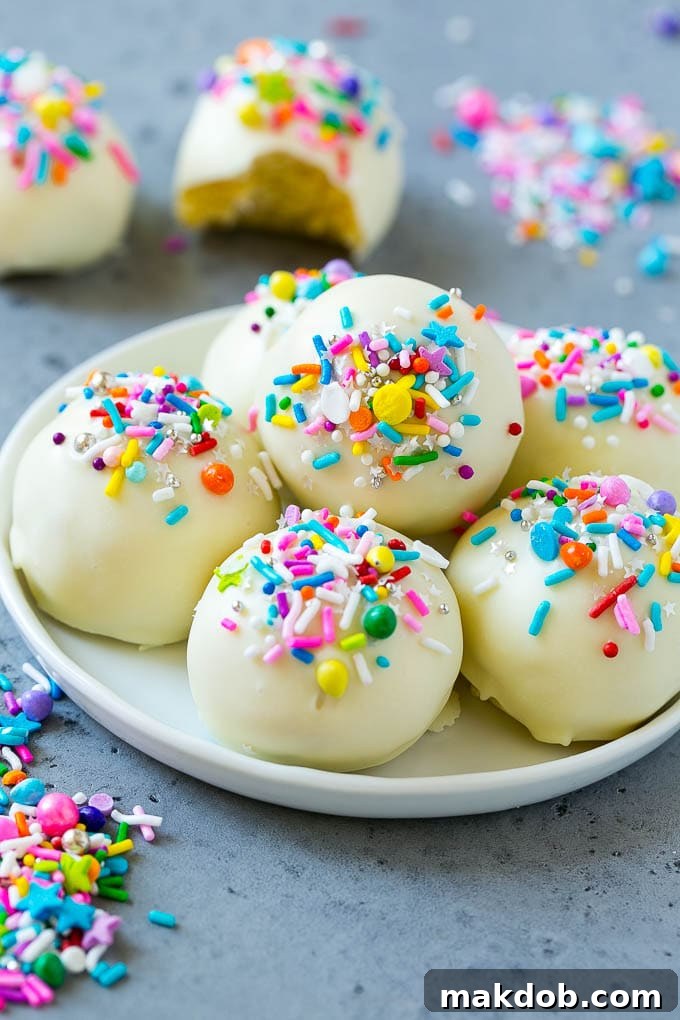 A plate of cake balls coated in white chocolate and rainbow sprinkles, showcasing the festive decoration.