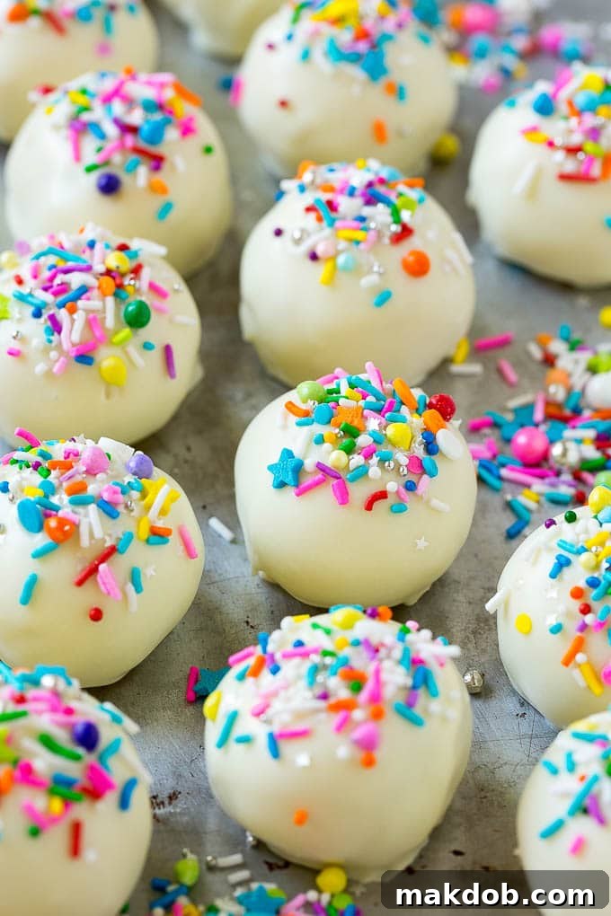Cake balls coated in white chocolate and colorful sprinkles, arranged on a sheet pan.