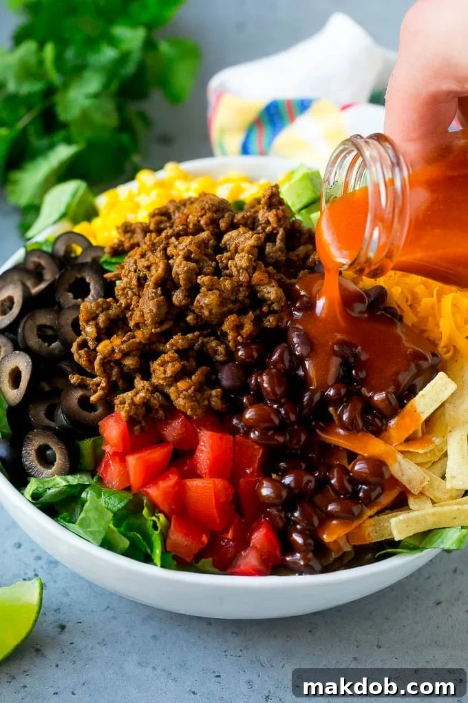 Taco Salad Recipe | Beef Taco Salad | Mexican Salad #salad #taco #beef #lunch #avocado #dinner #dinneratthezoo Catalina dressing being poured over taco salad.