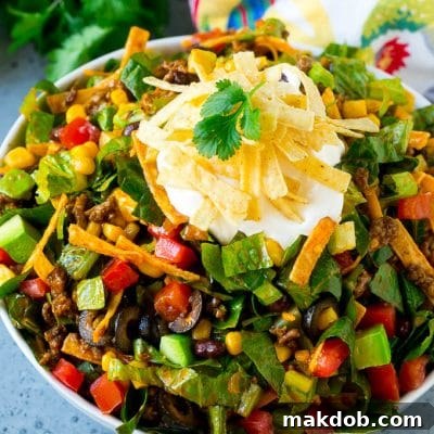 The Ultimate Taco Salad 2 Taco salad made with ground beef, romaine lettuce and vegetables, topped with sour cream and tortilla strips.