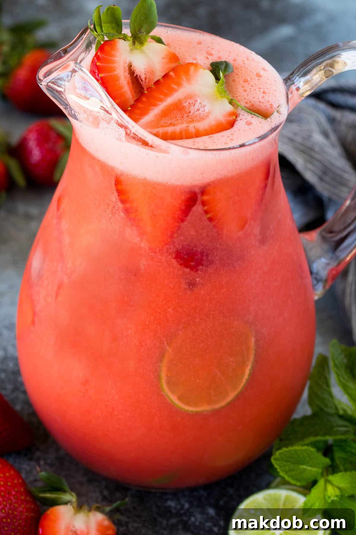 Luscious Strawberry Refresher 6 A glass pitcher filled with vibrant red strawberry agua fresca, garnished with fresh strawberries and lime slices.