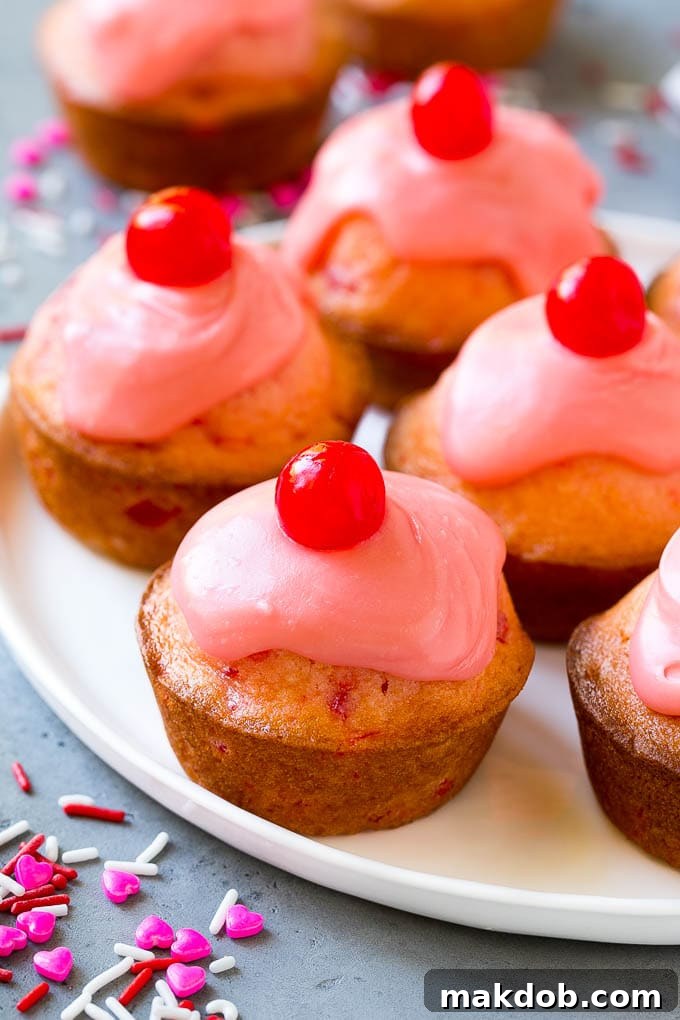 Cherry Muffins Recipe | Maraschino Cherry Muffins #cherries #cherry #muffins #baking #dessert #sweets #dinneratthezoo Cherry muffins on a plate, decadently topped with a pink glaze and a whole cherry, ready to be enjoyed.