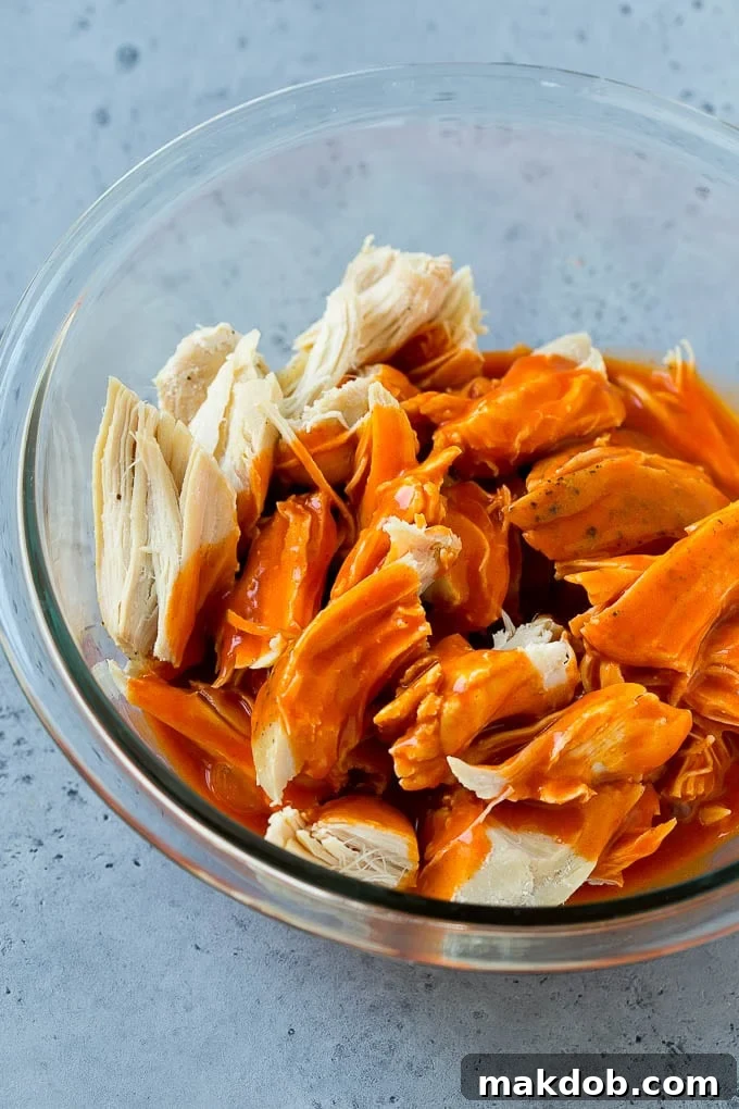 A bowl of freshly shredded chicken being drizzled with a rich, vibrant buffalo sauce, preparing it for the taco filling.
