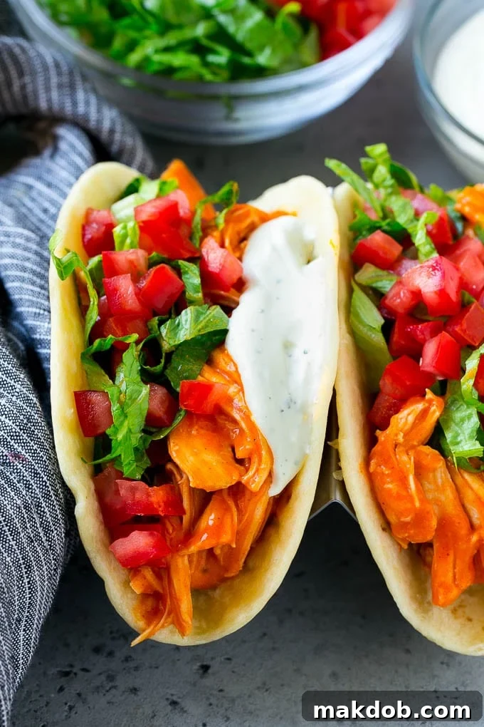 Three perfectly assembled buffalo chicken tacos, showcasing the shredded chicken, fresh lettuce, diced tomato, and a generous drizzle of creamy ranch sauce, arranged on a serving plate.