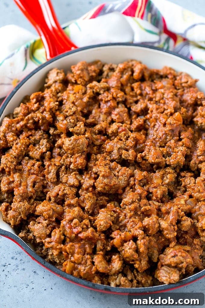 Ground beef taco meat simmering in a skillet with spices and tomato sauce.