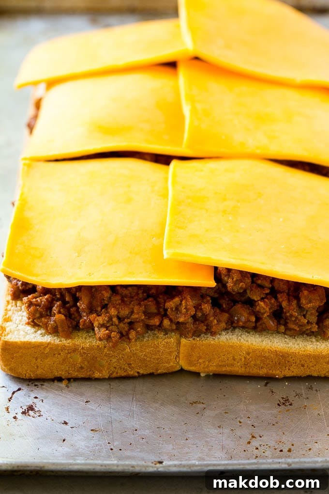 Ground beef and sliced cheddar cheese layered on top of toasted slider buns.