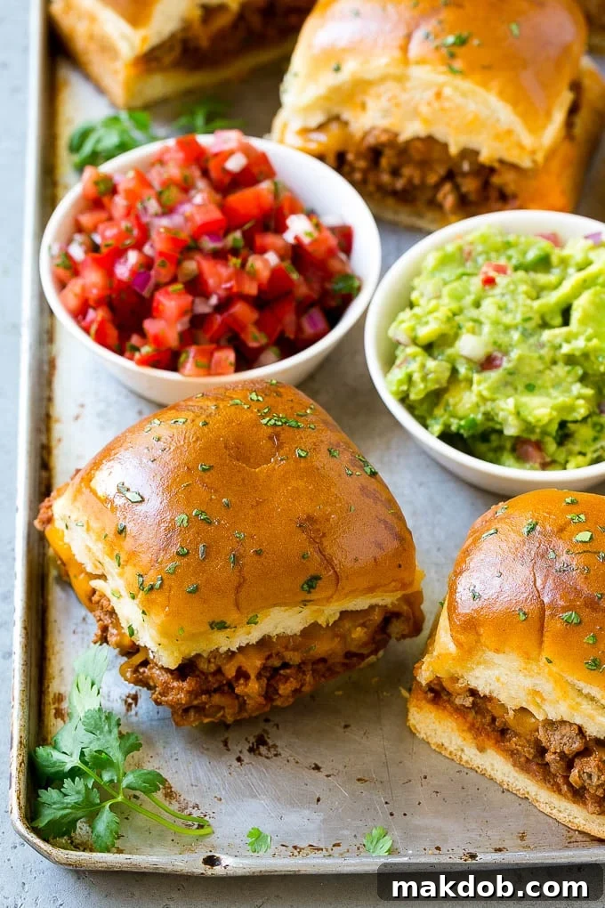 A tray of taco sliders filled with seasoned meat and melted cheese, served alongside bowls of guacamole and salsa.