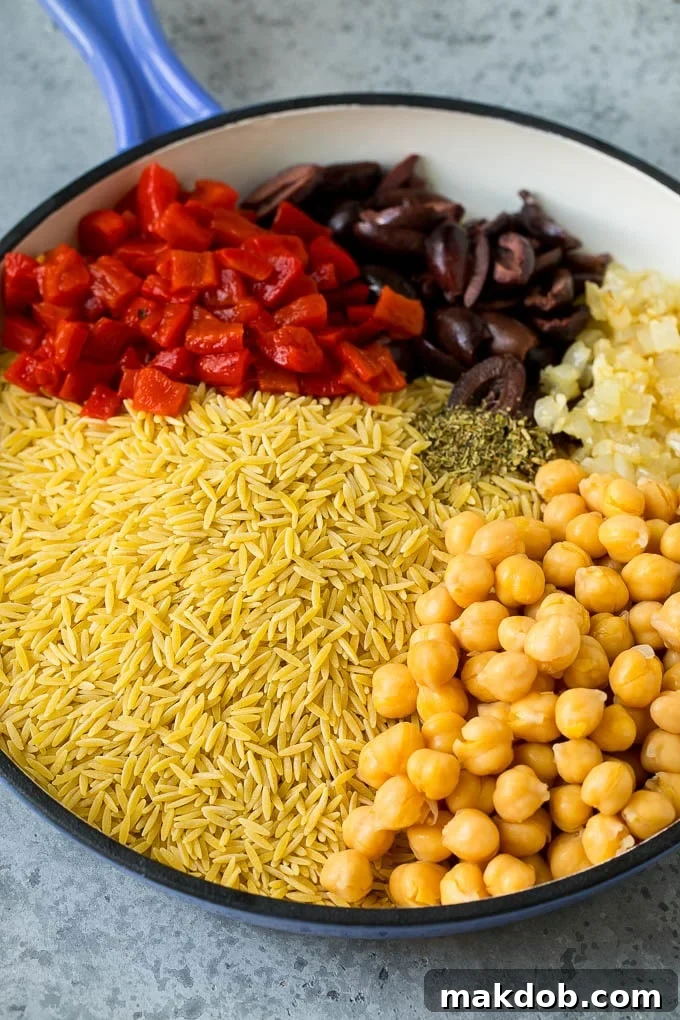 Orzo pasta, olives, chickpeas and roasted peppers in a skillet.