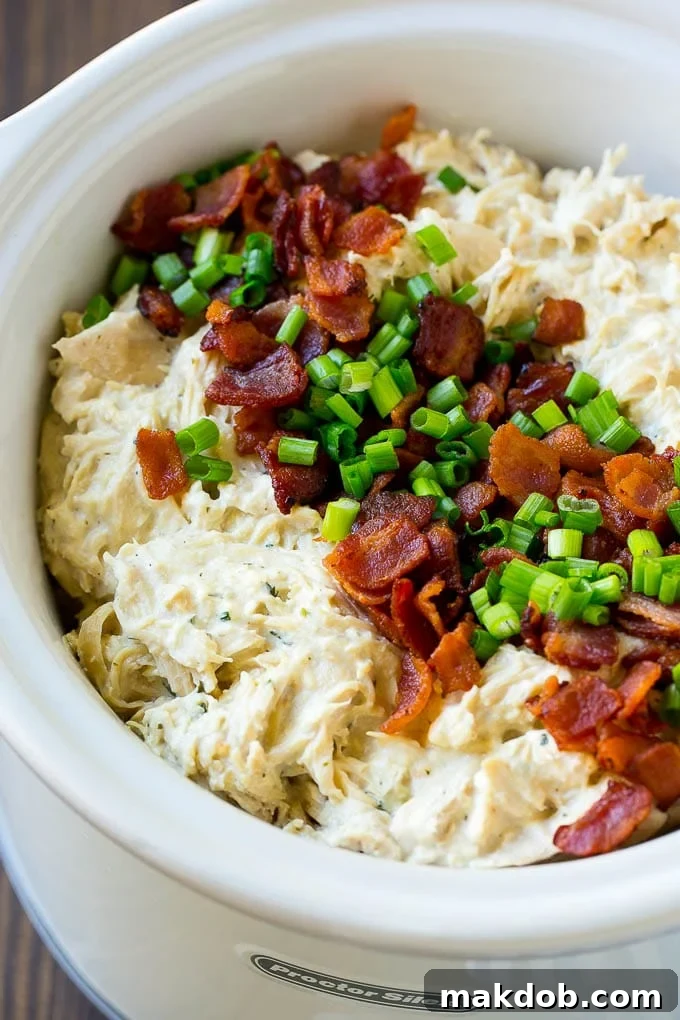 A slow cooker full of shredded crack chicken topped with bacon and sliced green onions.