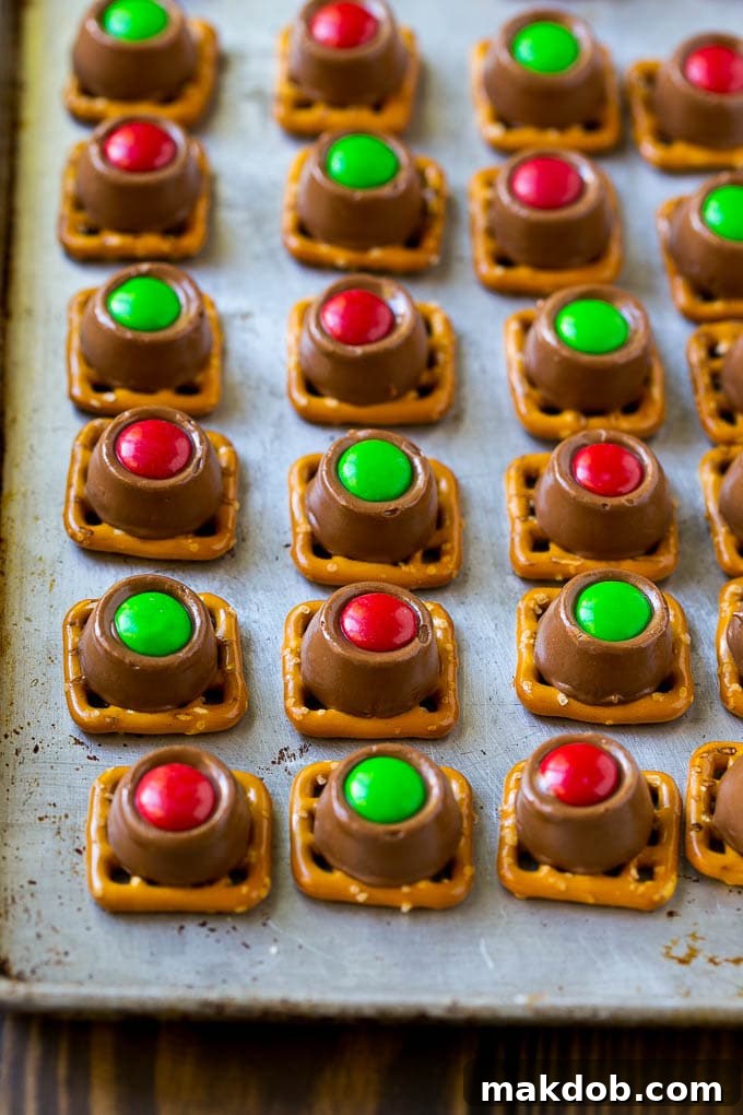 Rolo Pretzels Recipe | Chocolate Pretzels | Caramel Pretzels | Holiday Candy #christmas #baking #dessert #candy #chocolate #caramel #pretzels #dinneratthezoo A baking sheet filled with Rolo pretzels, freshly topped with vibrant red and green M&M's, cooling.