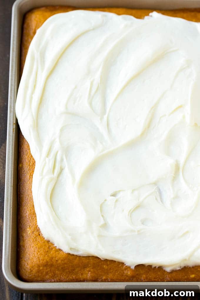 Cream cheese frosting being spread evenly over a baked pumpkin cake.