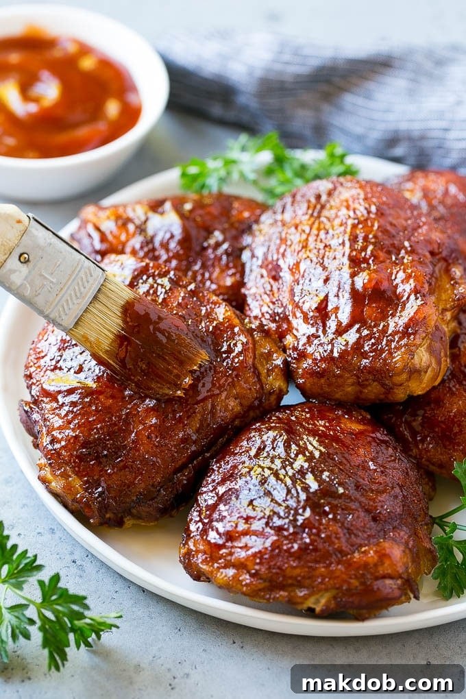 Juicy Smoked Chicken Thighs 5 A plate of smoked chicken thighs being basted with barbecue sauce, showcasing a beautiful glaze.