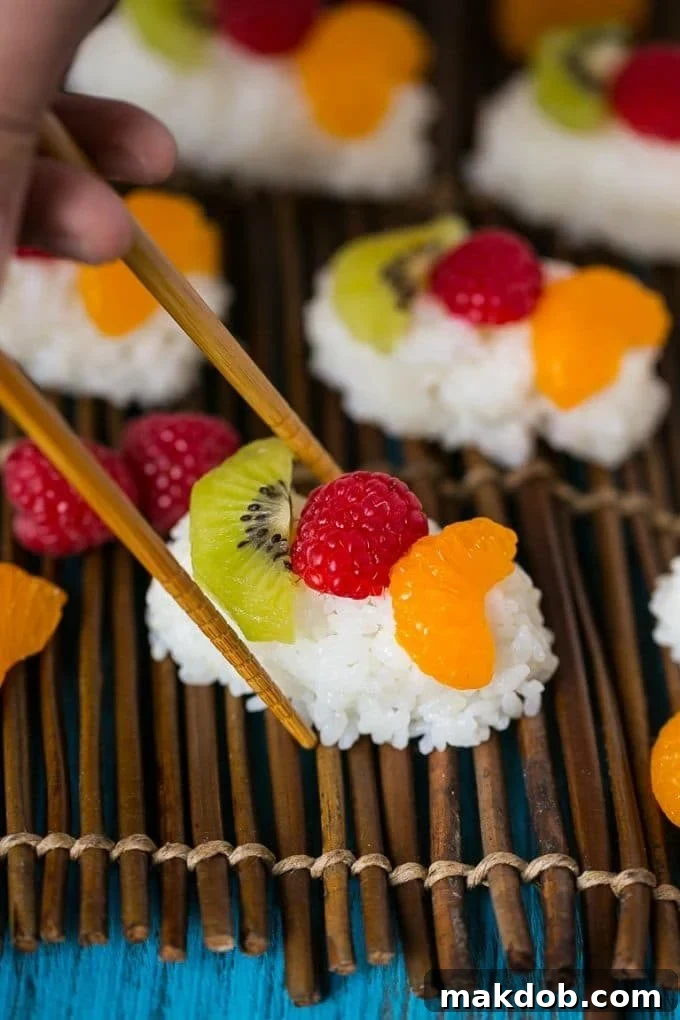 Chopsticks picking up a piece of fruit sushi.