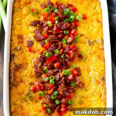 A casserole of loaded corn casserole topped with bacon, red peppers and green onions.