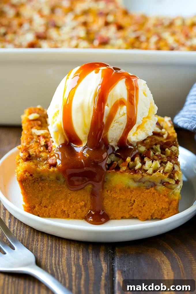 A generous slice of golden-brown pumpkin dump cake, crowned with a melting scoop of vanilla ice cream and glistening caramel sauce, ready to be enjoyed.