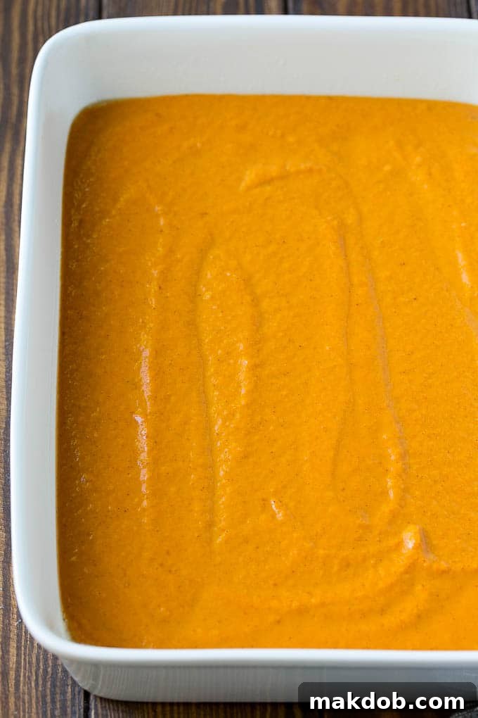Smooth, spiced pumpkin pie filling has just been poured into a glass baking dish, forming the vibrant orange base layer of the dump cake.