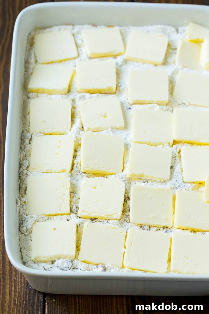 The dry yellow cake mix layer, dotted with thin slices of butter and a generous sprinkle of pecans, covers the pumpkin filling in the baking dish, awaiting the oven.