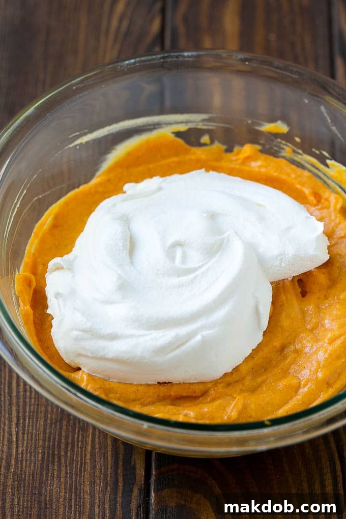 Cool whip being gently folded into the creamy pumpkin base for a fluffy dip.