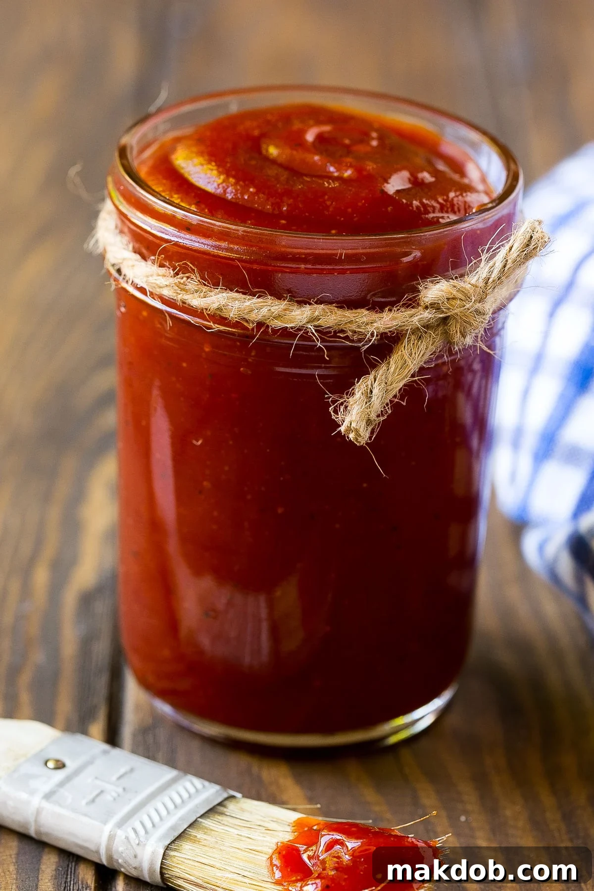 Signature Backyard BBQ Sauce 2 A charming glass jar filled with rich, homemade BBQ sauce, with a basting brush resting beside it, symbolizing readiness for grilling.