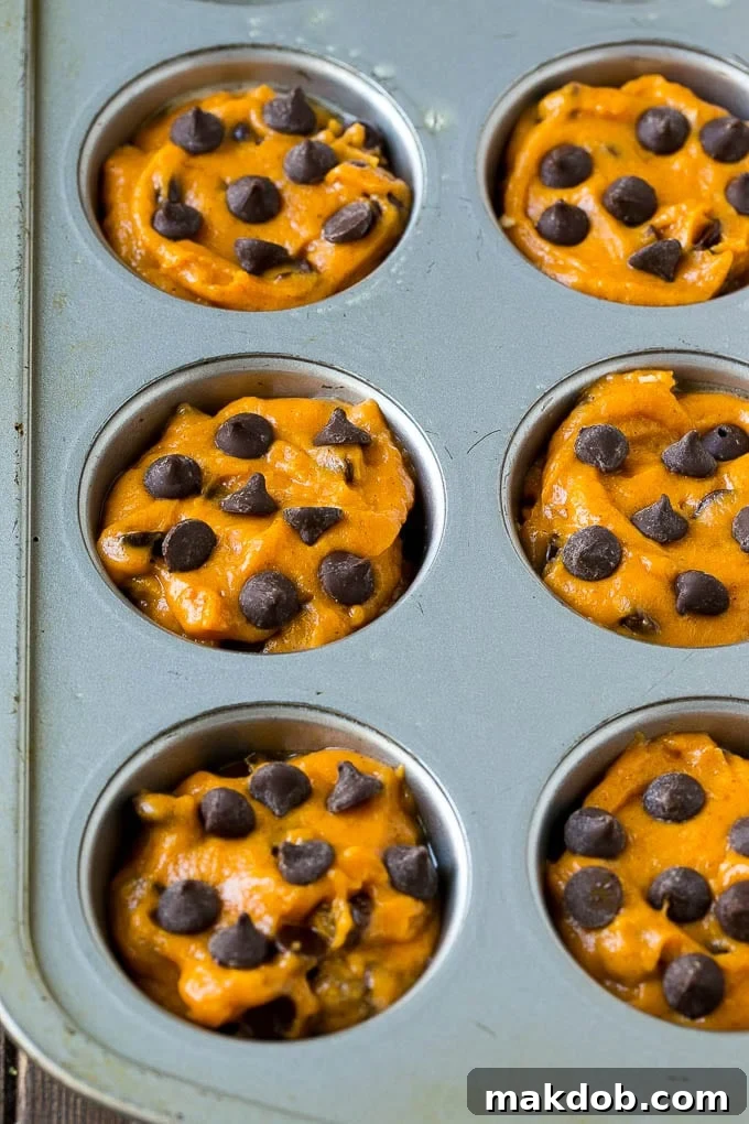 Pumpkin muffin batter carefully scooped into paper-lined muffin tins, ready for baking.