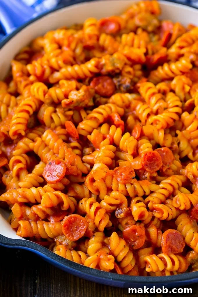 Close-up of rotini pasta cooked to perfection with pepperoni and a rich tomato sauce, ready to be topped with cheese.