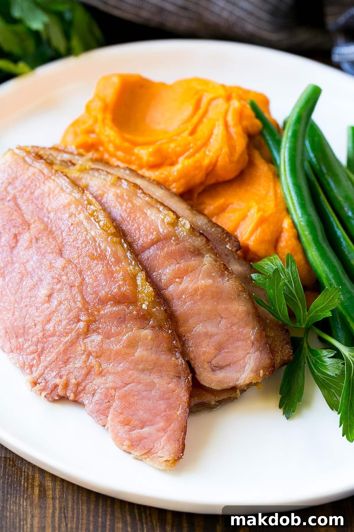Sliced ham served on a plate with creamy mashed sweet potatoes and fresh green beans.