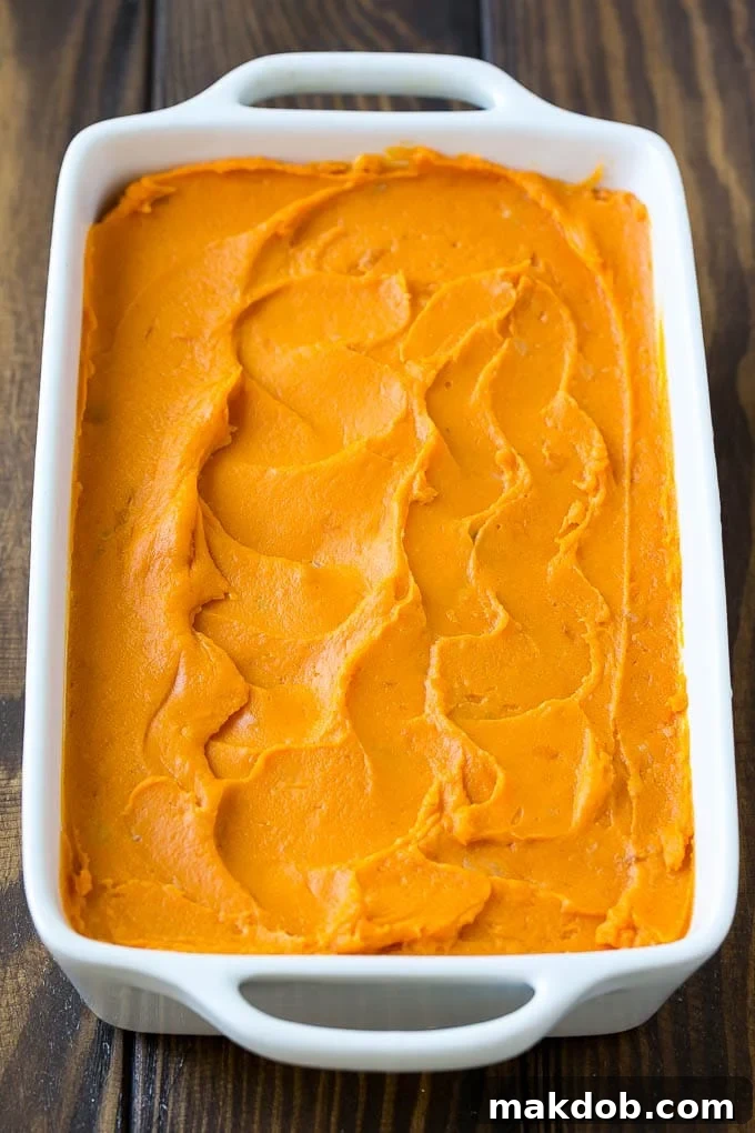 Creamy mashed sweet potatoes evenly spread in a baking dish, before the topping is added.