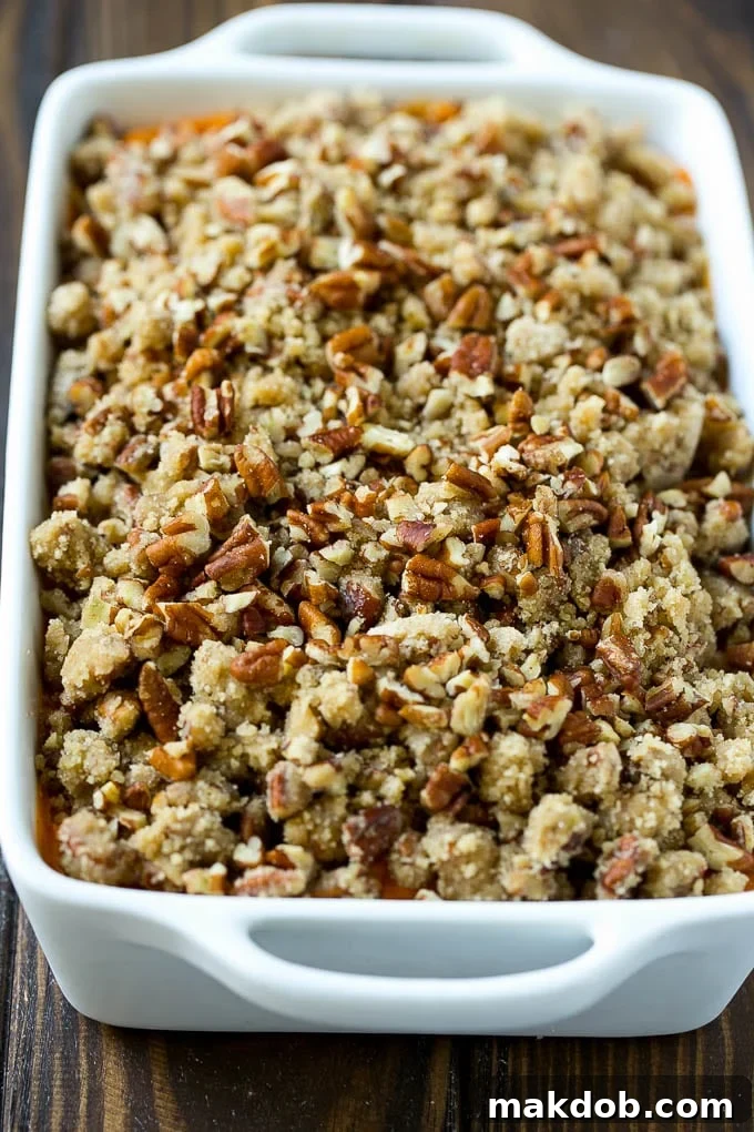 An uncooked sweet potato casserole with its pecan streusel topping, ready for the oven.