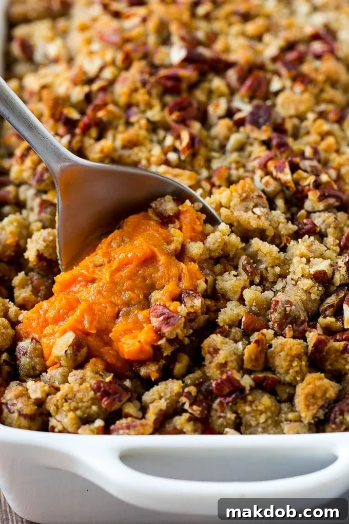 A serving of sweet potato casserole with a golden pecan streusel, topped with a spoon, ready to be enjoyed.