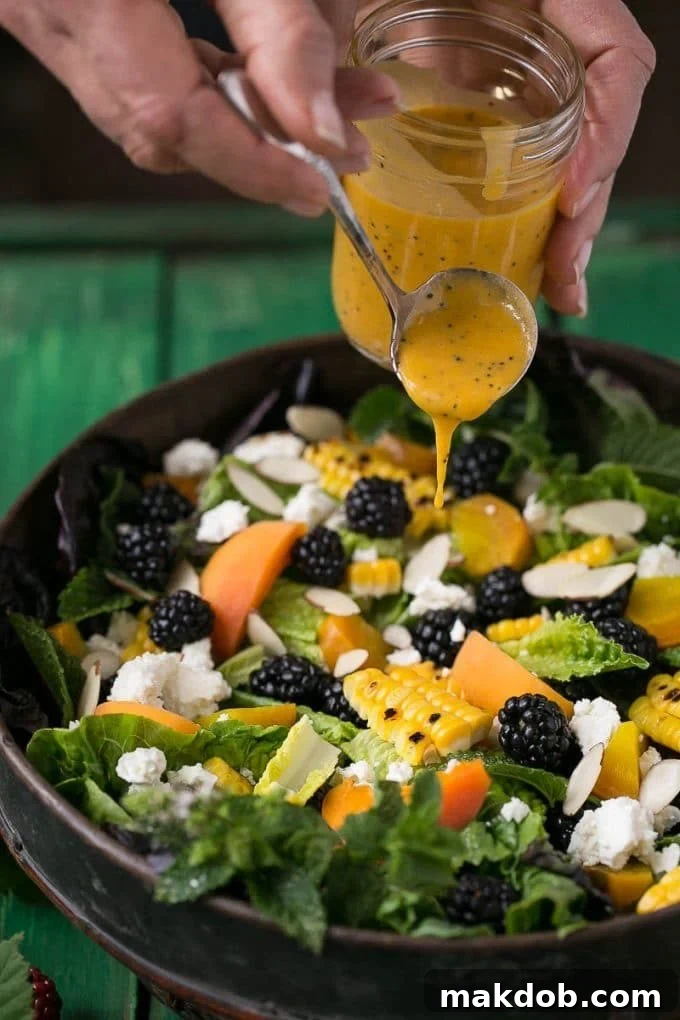 A hand gently spooning the creamy apricot poppy seed dressing over a colorful blackberry apricot salad, showcasing its luscious texture.