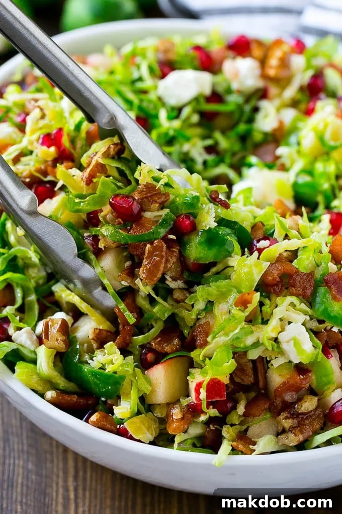 A bowl of brussels sprout salad with tongs picking some up out of the bowl.