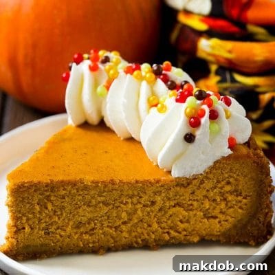 A slice of pumpkin cheesecake on a graham cracker crust, topped with whipped cream and sprinkles.