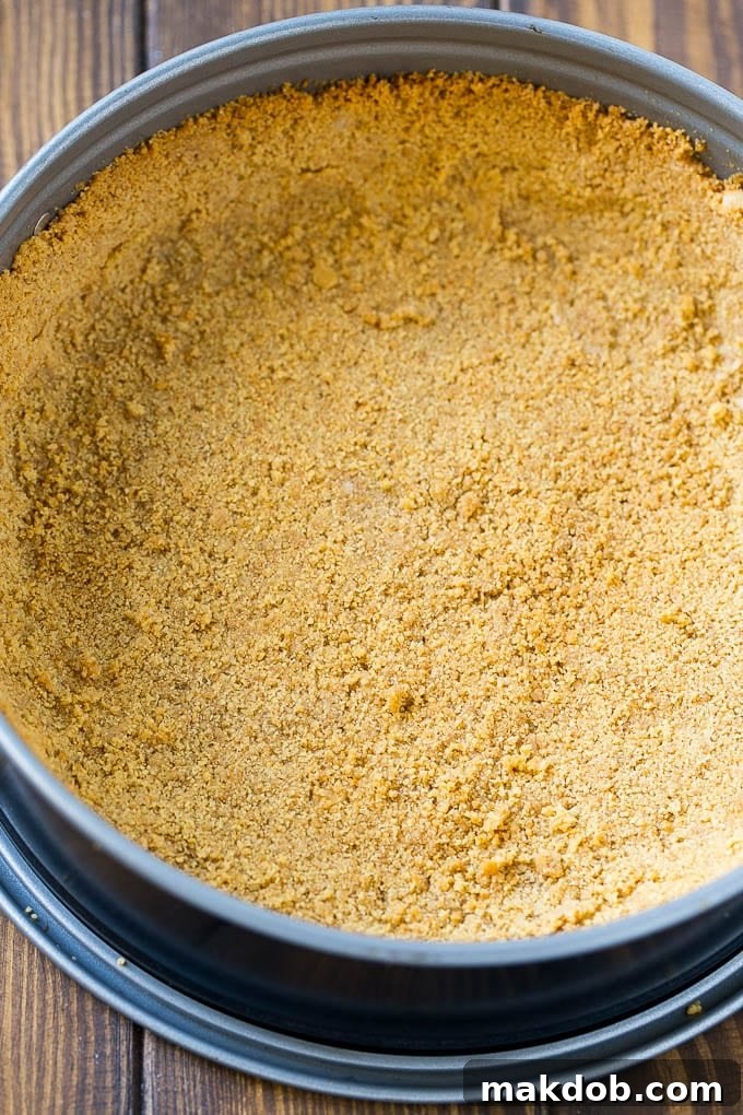 Pumpkin Cheesecake Graham Cracker Crust Preparation Graham cracker crumbs mixed with sugar and melted butter being pressed firmly into the bottom and sides of a springform pan.
