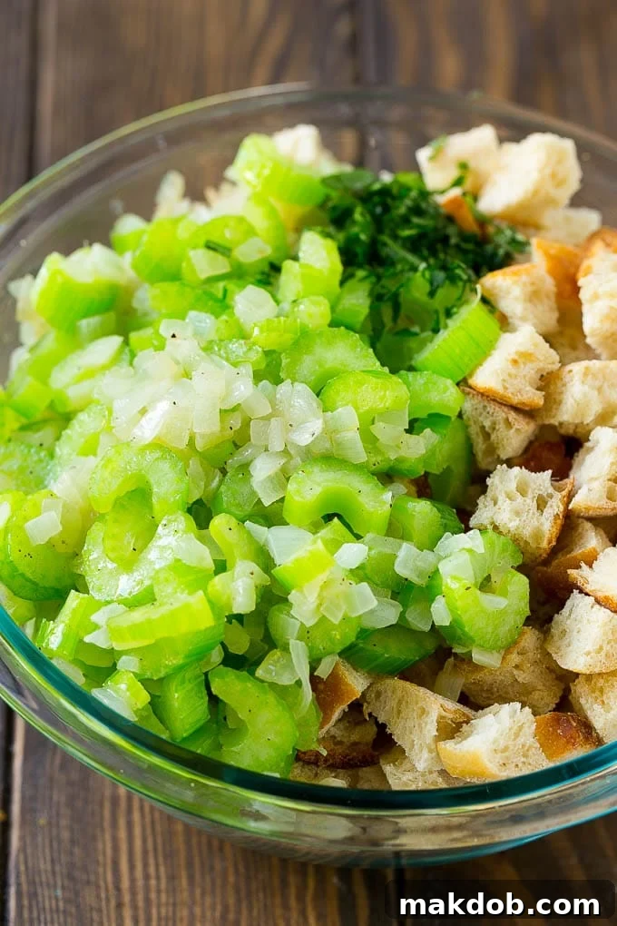 Bread cubes, celery, onion and fresh herbs in a mixing bowl for homemade stuffing.