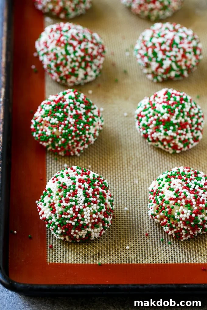 Balls of gooey butter cookie dough generously rolled in colorful sprinkles, arranged on a baking sheet.
