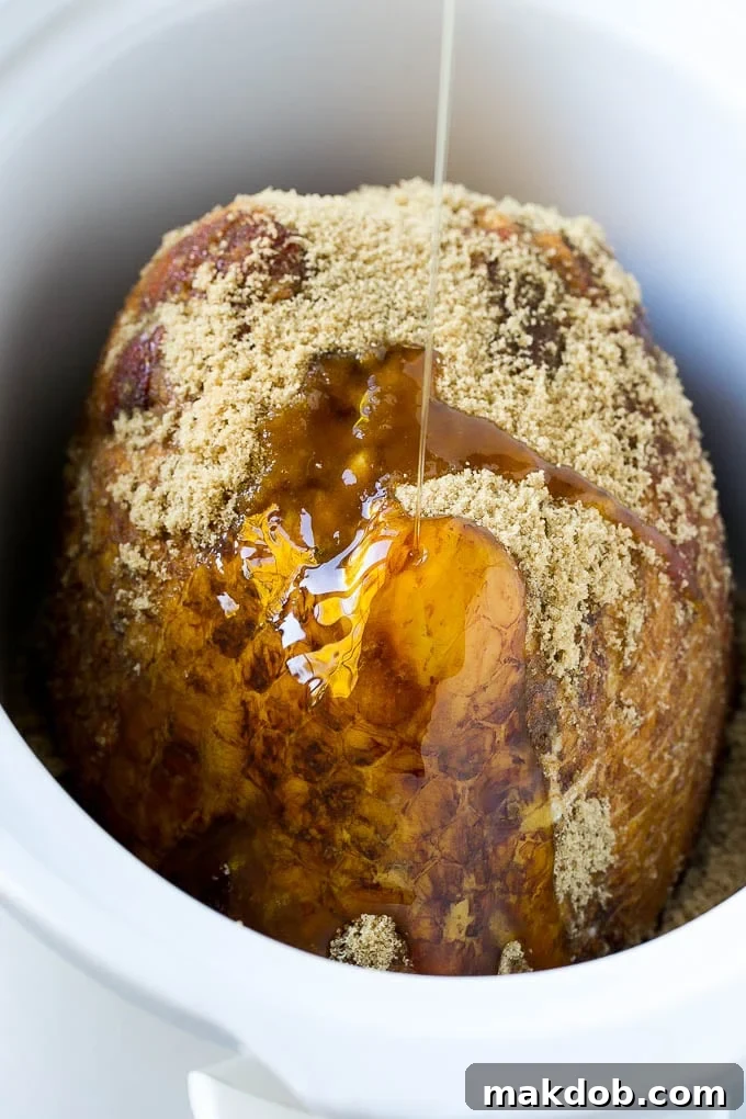 A crock pot ham with maple syrup being poured over the top.