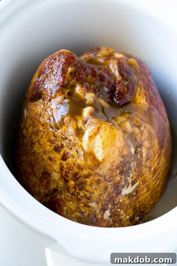 A ham in a slow cooker covered in brown sugar, maple syrup and pineapple juice.