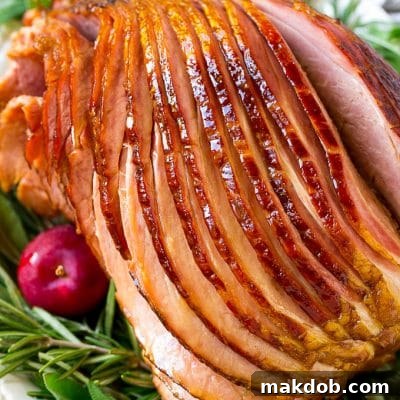 A crock pot ham on a serving plate with herbs and apples for garnish.