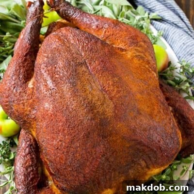 Smoked turkey on a platter garnished with herbs and apples.