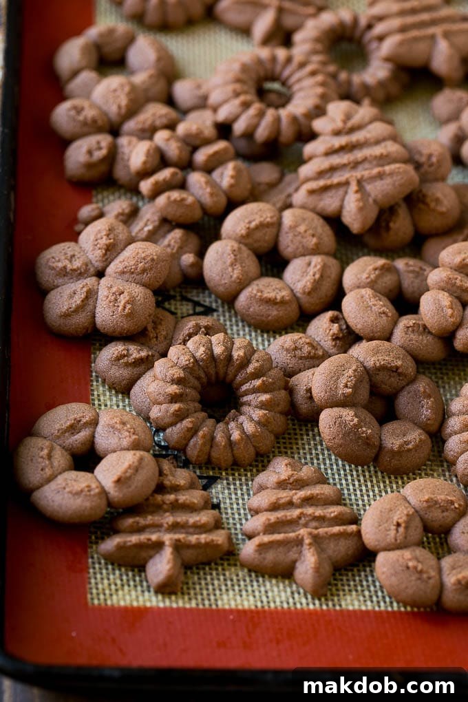 Freshly baked chocolate spritz cookies cooling on a wire rack on a sheet pan.