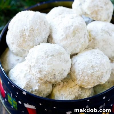 Snowball cookies coated in powdered sugar and served in a holiday tin, representing the perfect festive treat.