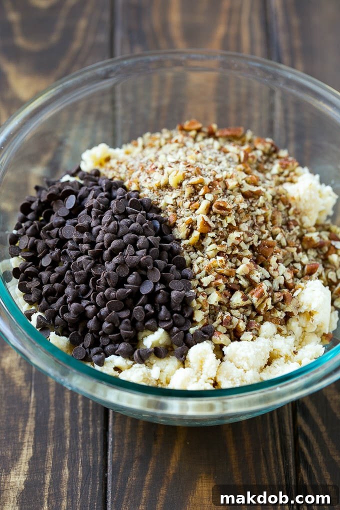 Snowball Cookies Recipe | Mexican Wedding Cookies | Russian Tea Cakes #cookies #pecan #chocolate #baking #dessert #christmas #dinneratthezoo A bowl filled with a crumbly cookie dough, visibly mixed with miniature chocolate chips and finely chopped pecans, ready for shaping.