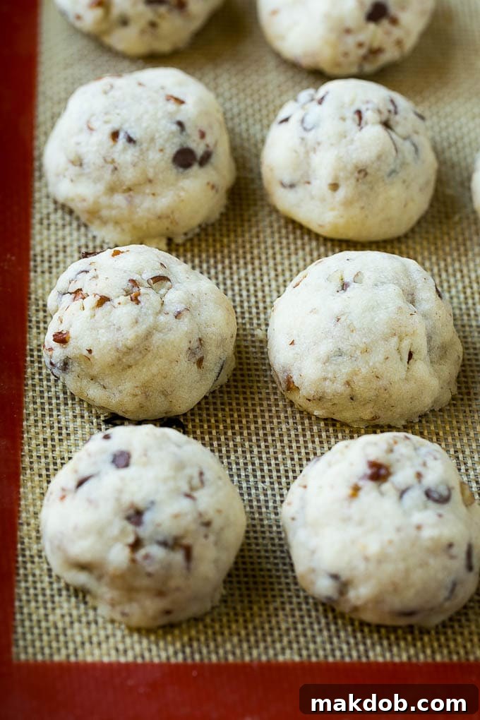 Snowball Cookies Recipe | Mexican Wedding Cookies | Russian Tea Cakes #cookies #pecan #chocolate #baking #dessert #christmas #dinneratthezoo Freshly baked snowball cookies, lightly golden at the edges, resting on a sheet pan after their first dusting of powdered sugar.
